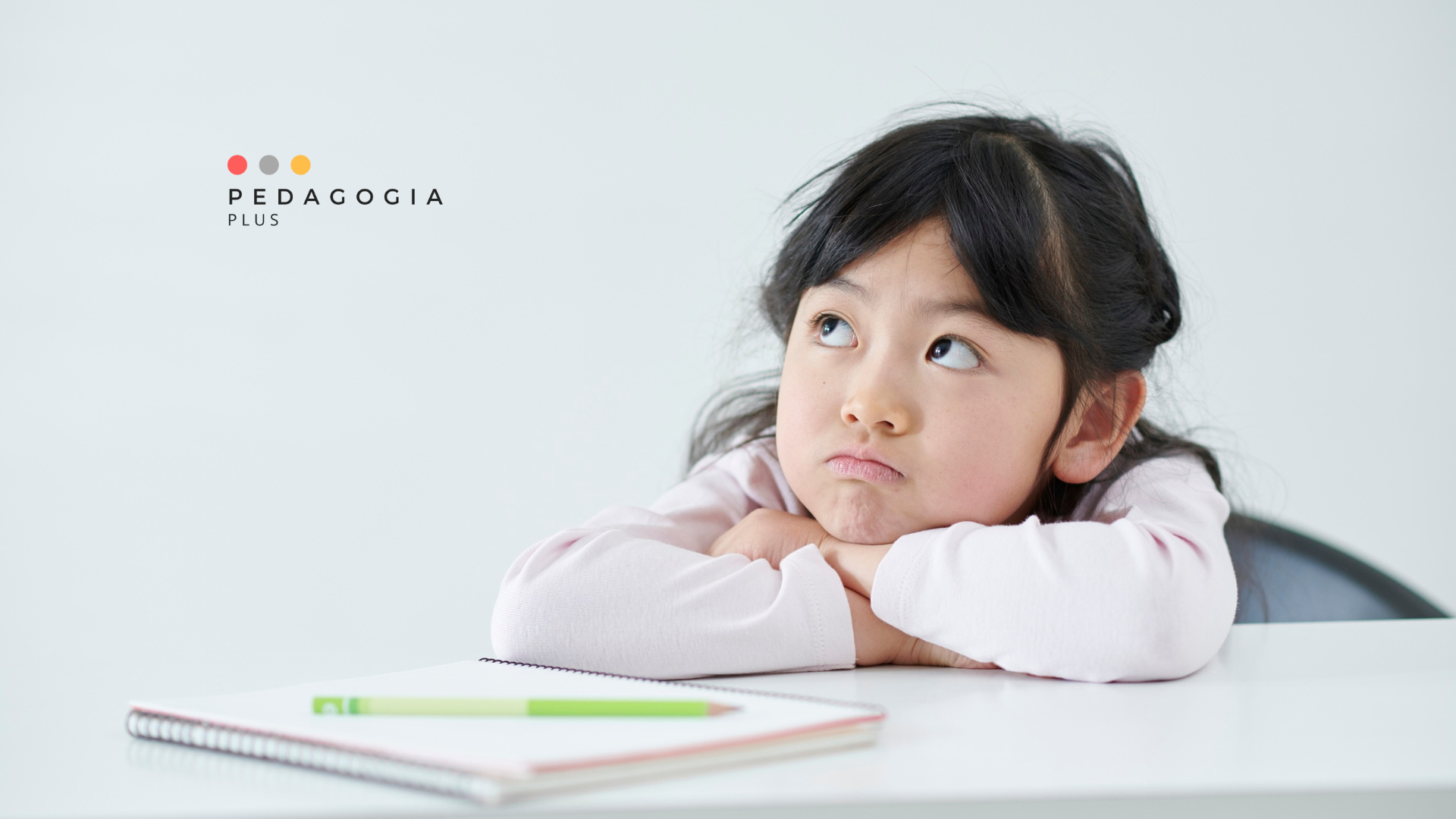 bambina a braccia incrociate e broncio davanti a un quaderno e  una penna