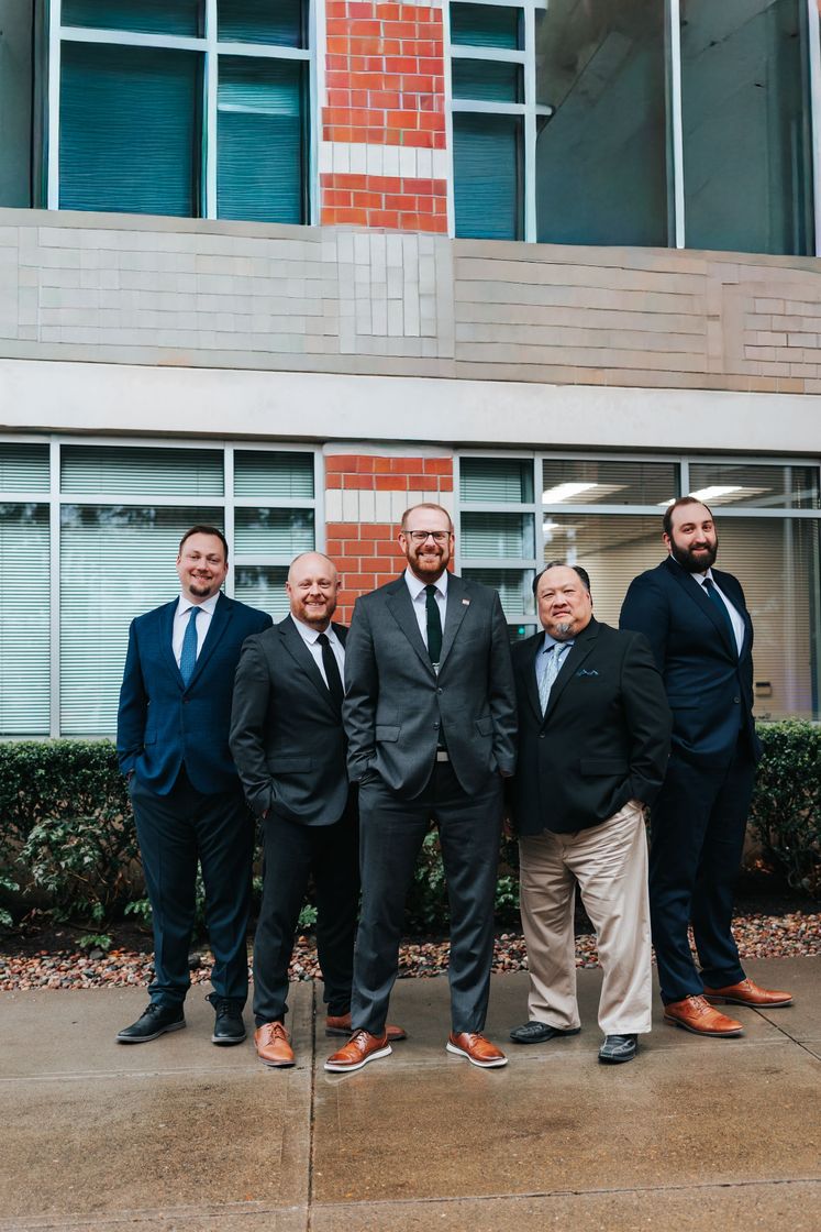 Group of nine people posing in front of a building. They are wearing business casual attire.