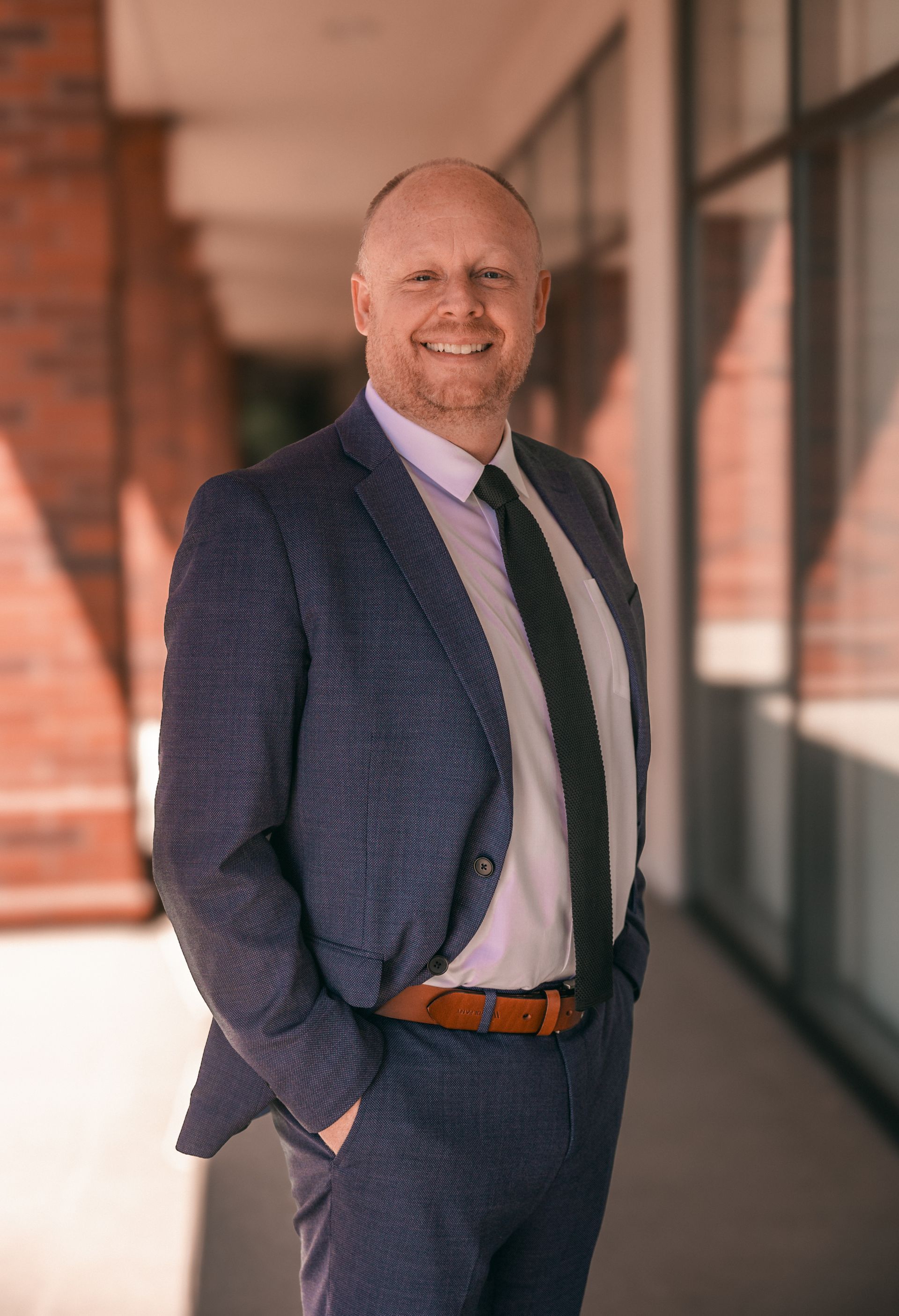 Man in blue suit, smiling, standing outside with hands in pockets.