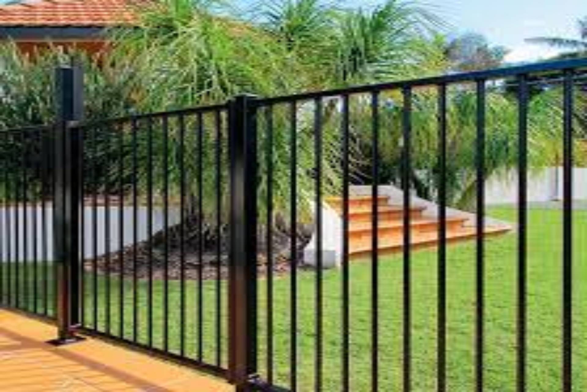 Black metal fence in a yard with green grass and foliage.
