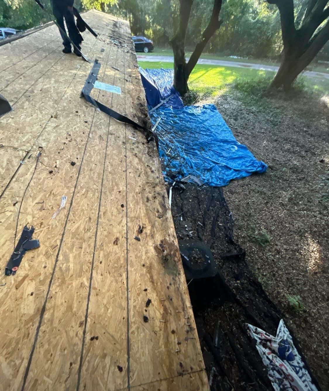 Roof being repaired with exposed wood, blue tarp, and debris. Roof being repaired with exposed wood, blue tarp, and debris.