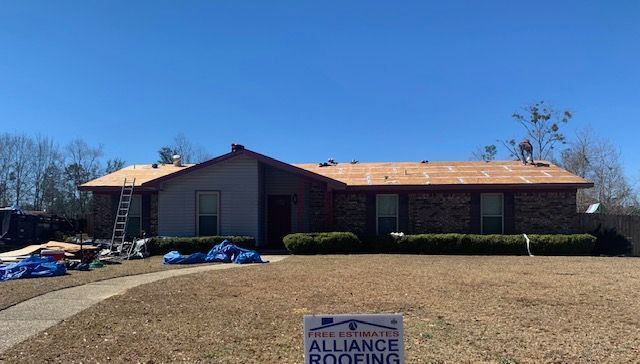 Roofers working on a residential roof, sunny day, blue tarp, sign in foreground.