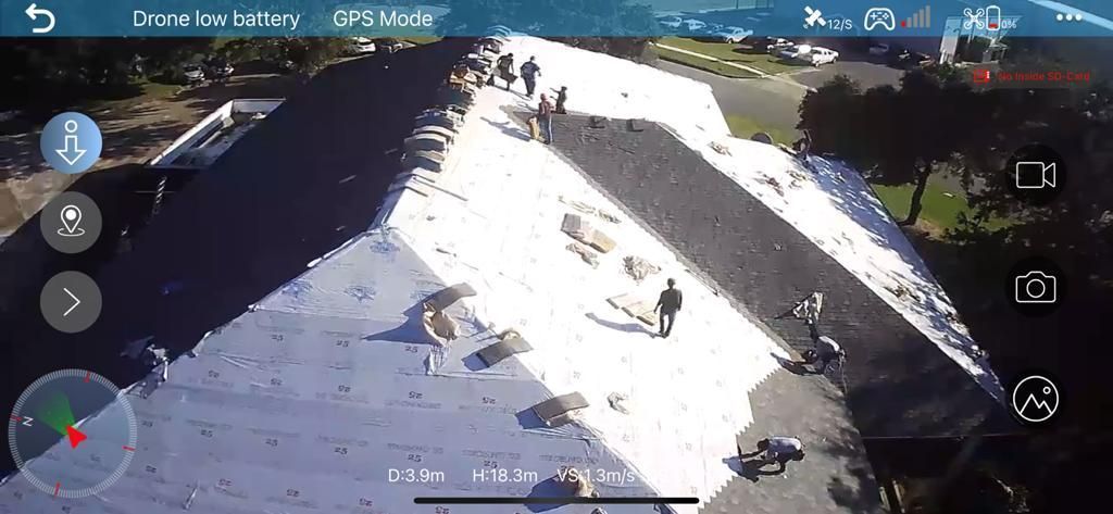Drone view of a white, angled roof with several people walking on it, next to a parking lot.