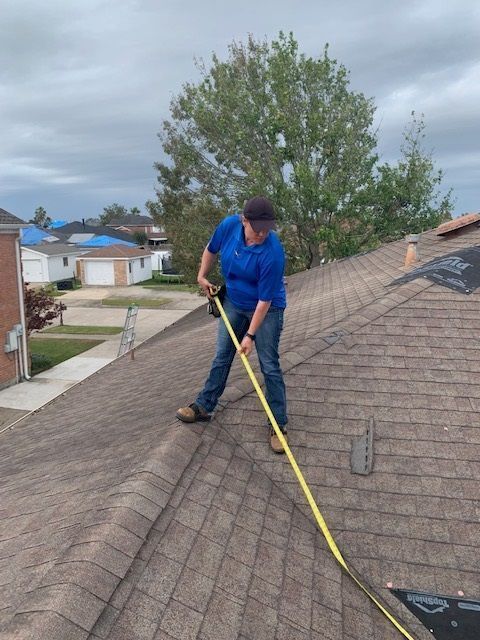 Person on a roof measuring with a yellow tape measure, brown shingles, cloudy sky.