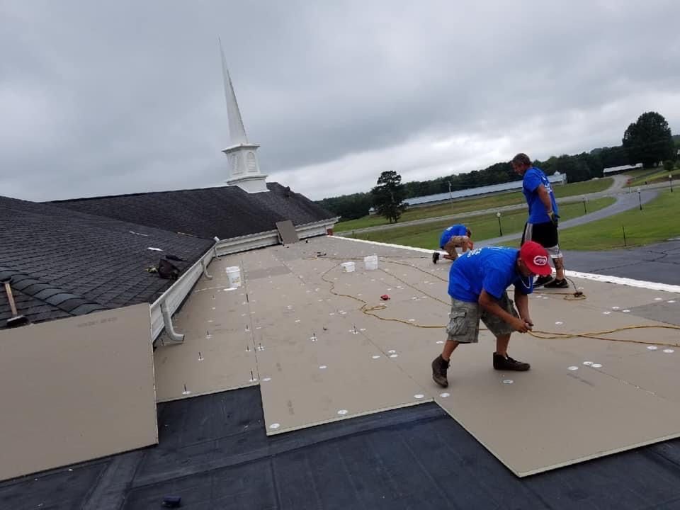 Roofers in blue shirts working on a roof near a church steeple. Cloudy day.