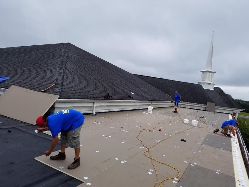 Roofers installing new roofing material on a dark roof under an overcast sky.