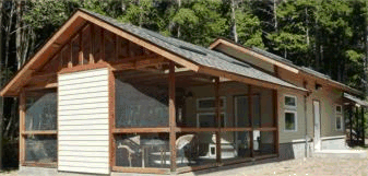 A cabin with a screened-in porch and wood siding, surrounded by trees.