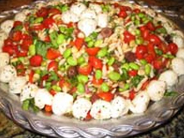 A pasta salad with tomatoes , onions and basil in a white bowl.