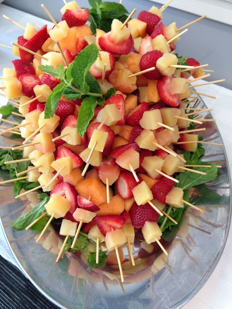A plate of fruit on skewers with mint leaves