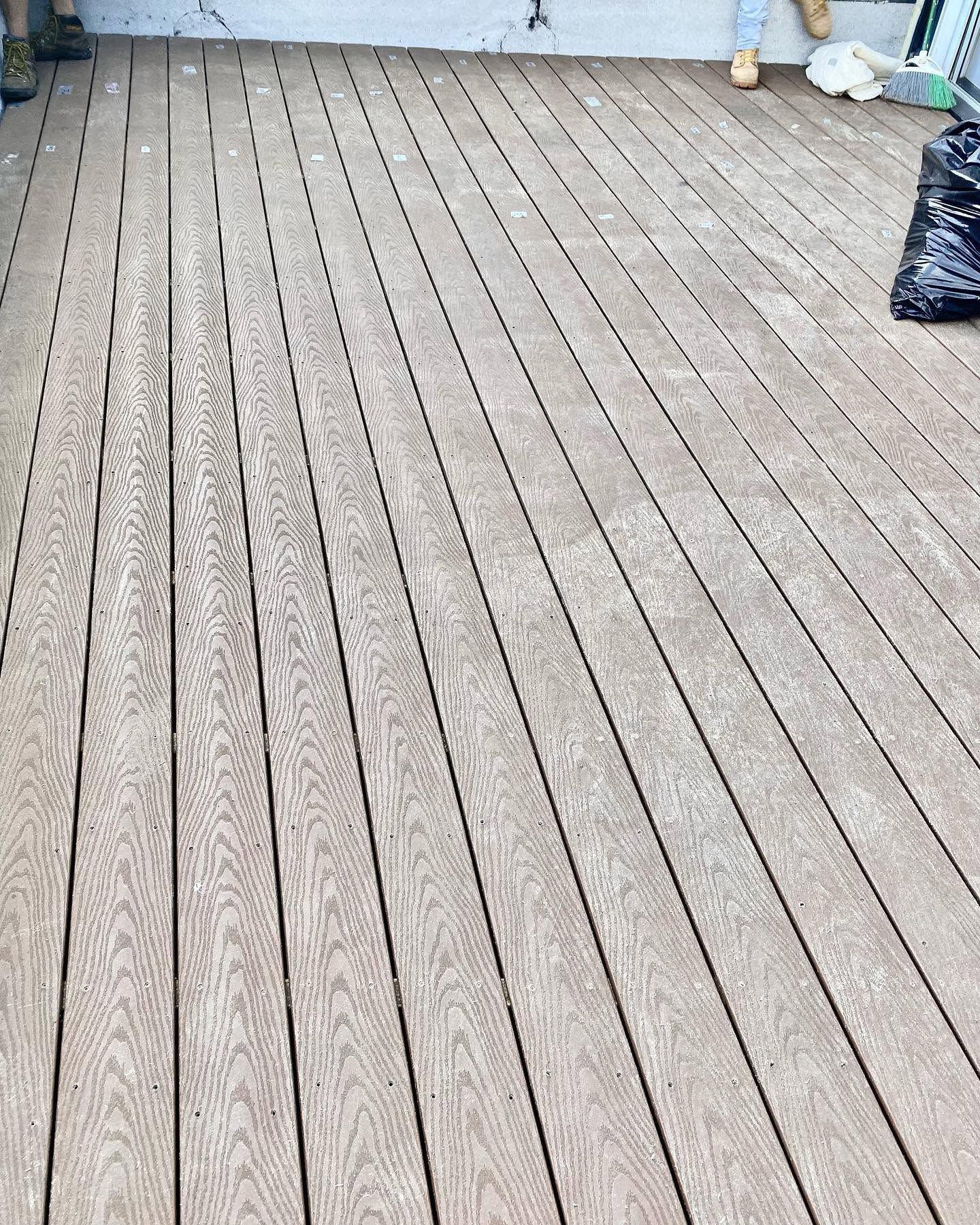 Empty wooden deck with long gray planks and a few small items near the back wall.