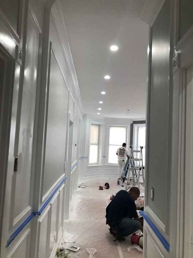 Hallway under renovation with workers, ladders, plastic sheeting, and tools on the floor