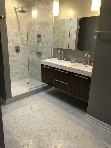 Modern bathroom with walk-in shower, floating vanity, large mirror, and pendant lights.
