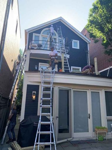 Worker on ladder painting the upper front of a blue house with white trim