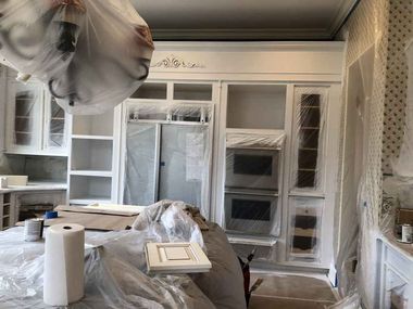 Painted room with taped plastic coverings over cabinets, windows, and a table during renovation