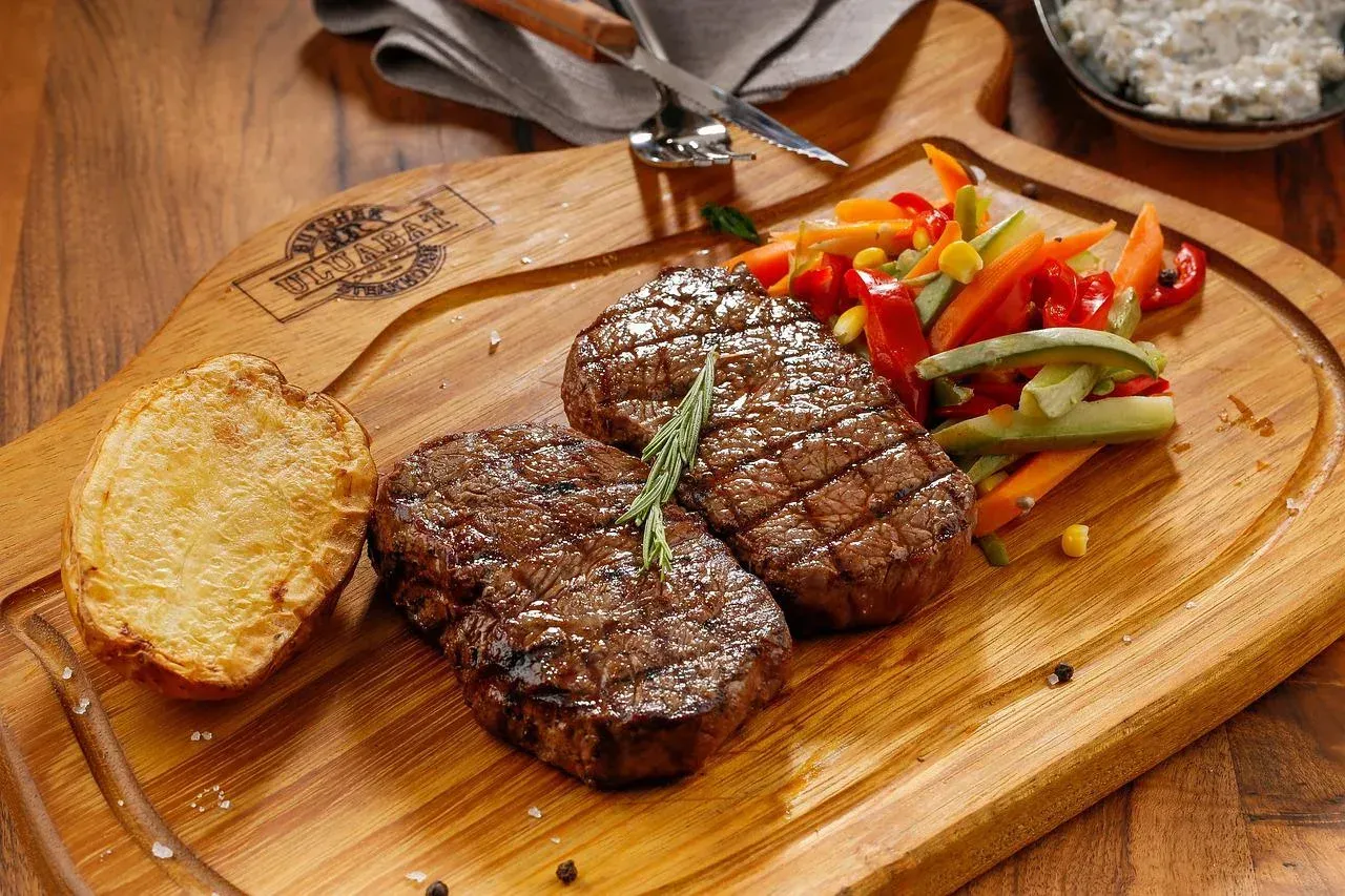 a wooden cutting board with a steak and vegetables on it