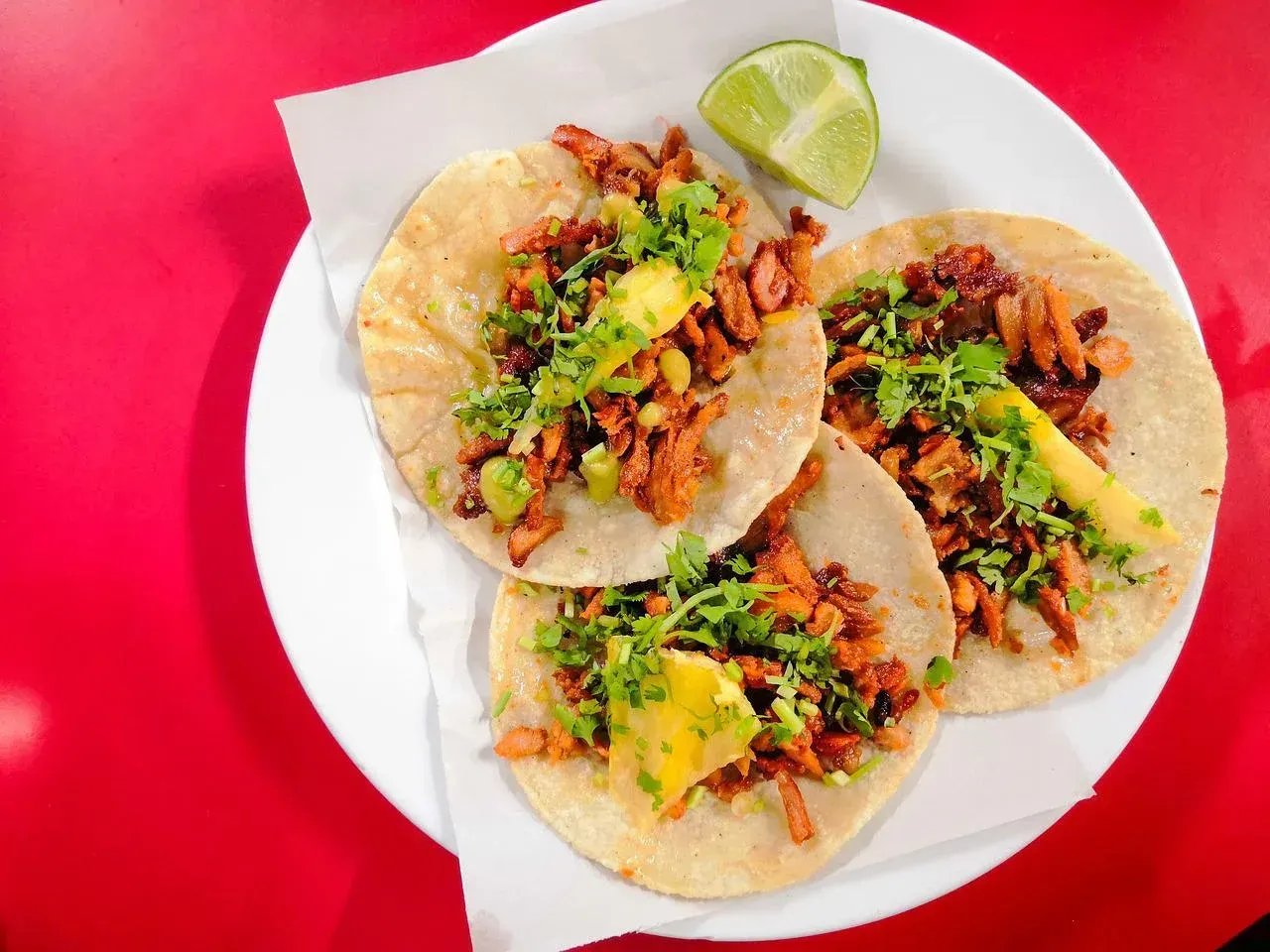 three tacos on a white plate with a lime wedge