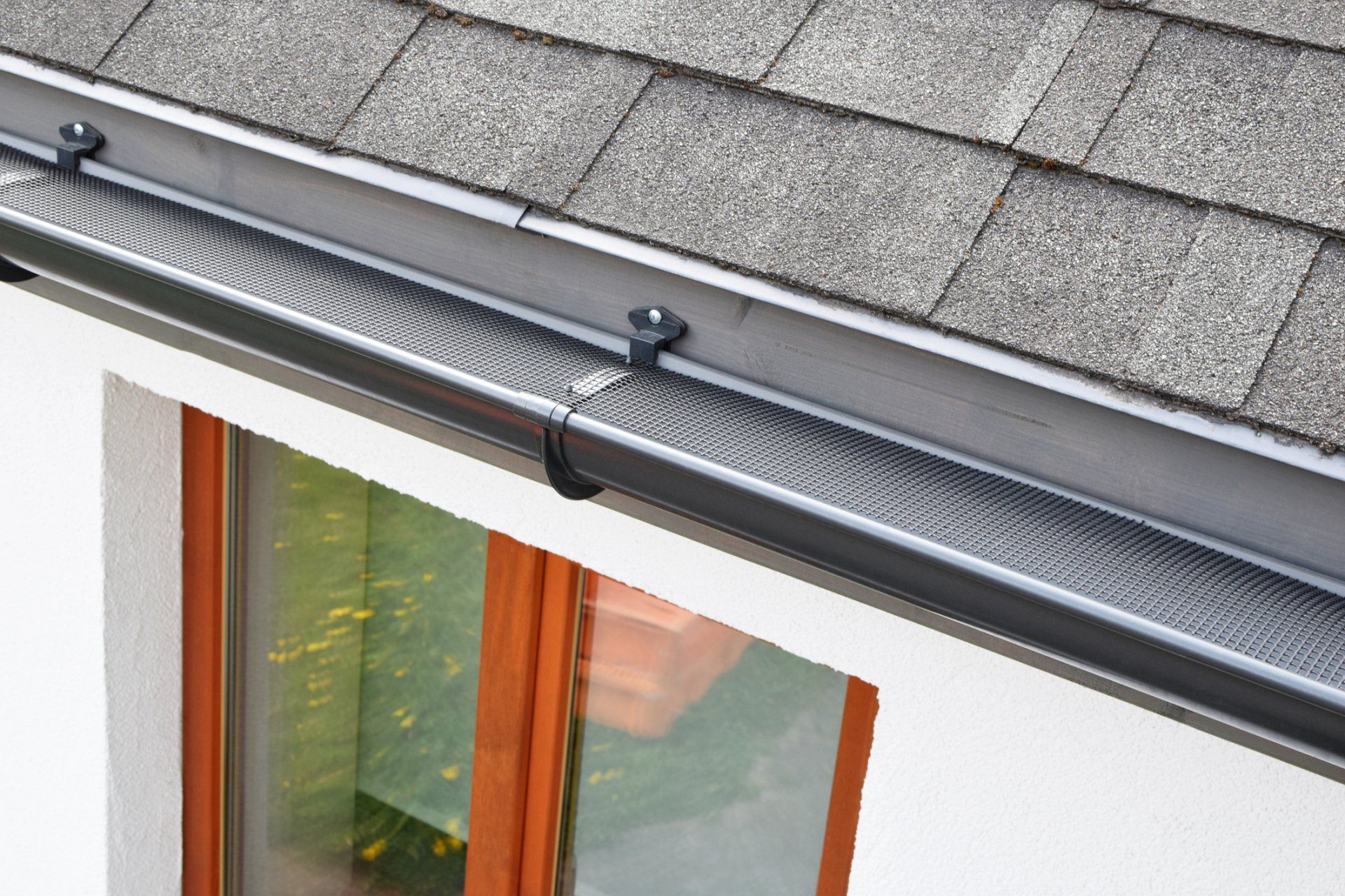 Roof gutter with leaf guard and downspout above a house window
