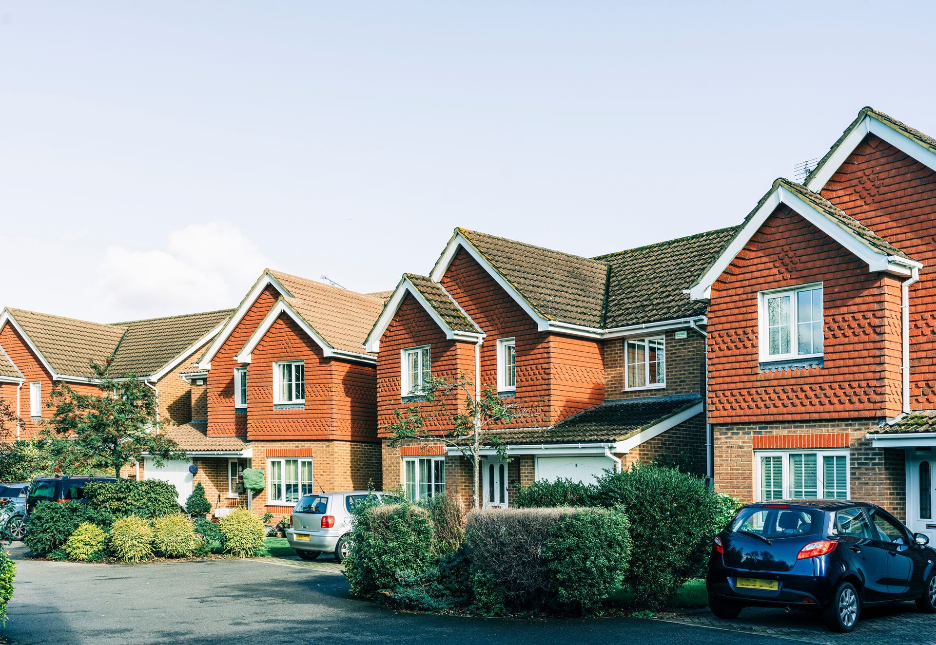 Row of brick houses with cars parked in front, on a sunny day.