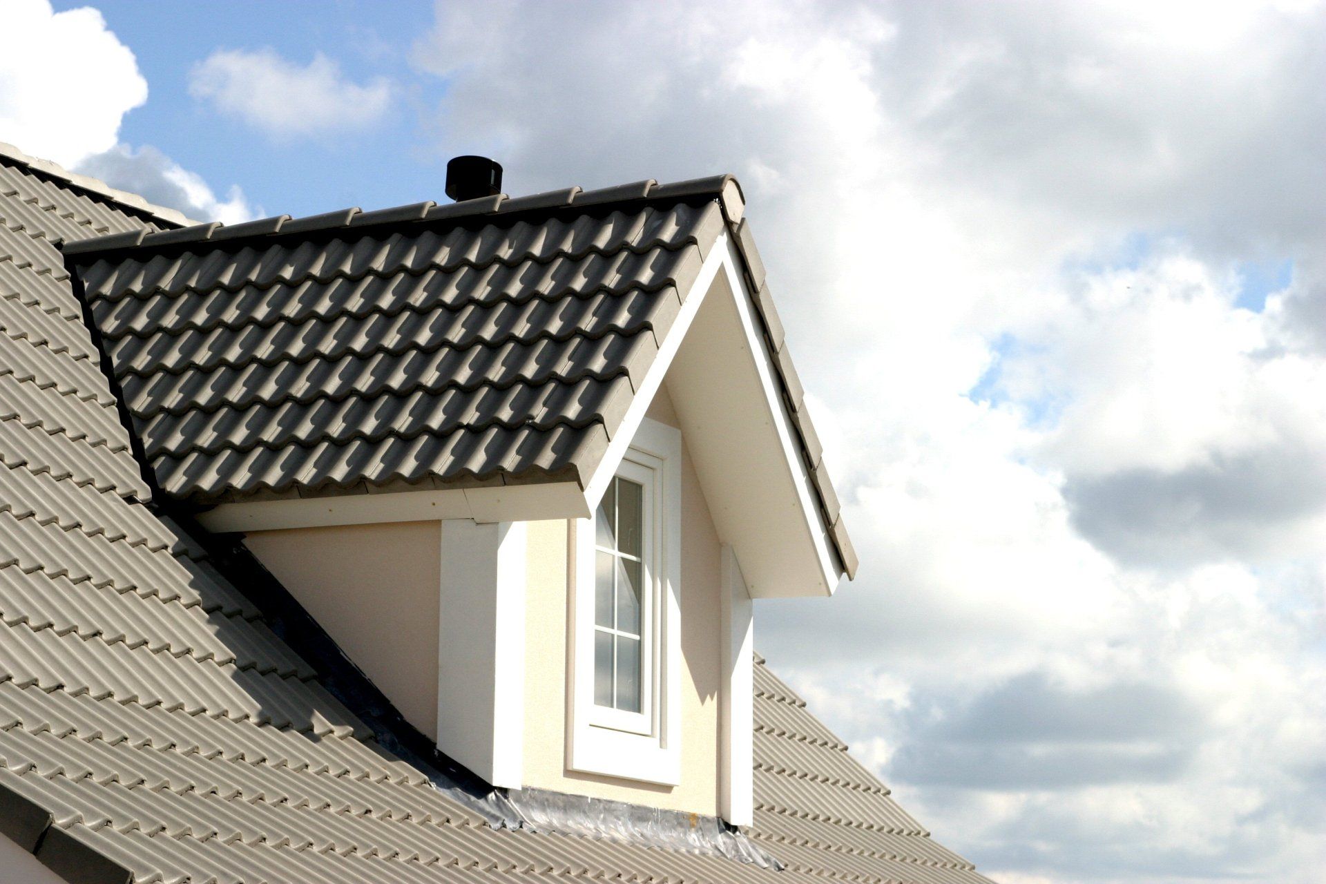 Dormer window with dark tiled roof against a cloudy sky
