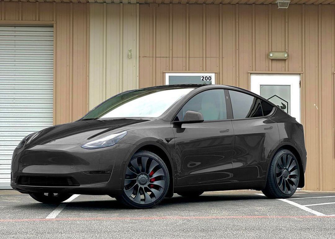 Dark gray Tesla Model Y parked in front of a building with brown siding and white doors.