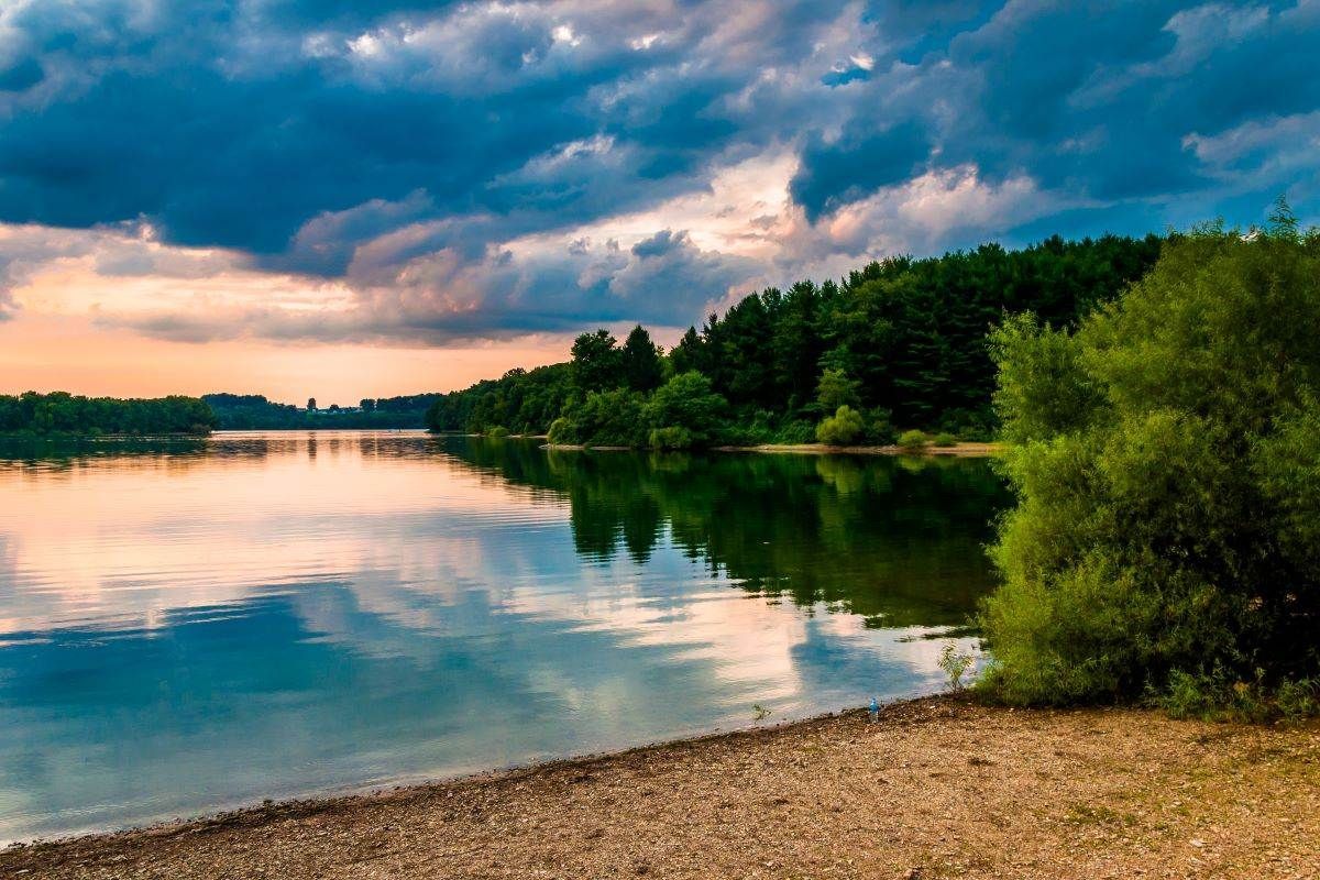 Calm lake reflects a cloudy sky and green trees at the shore.