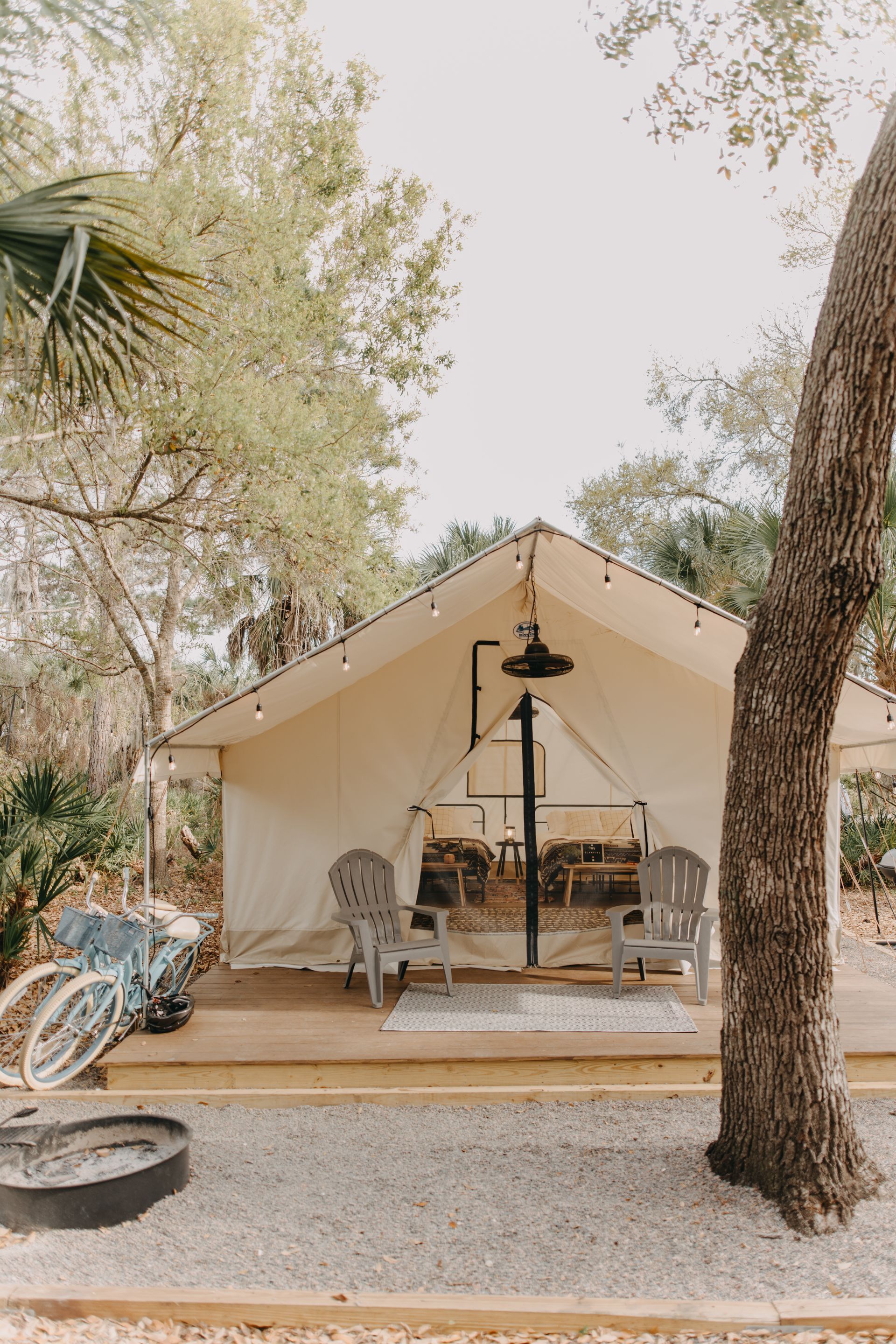Glamping tent with wooden deck and chairs, gravel ground, and trees.