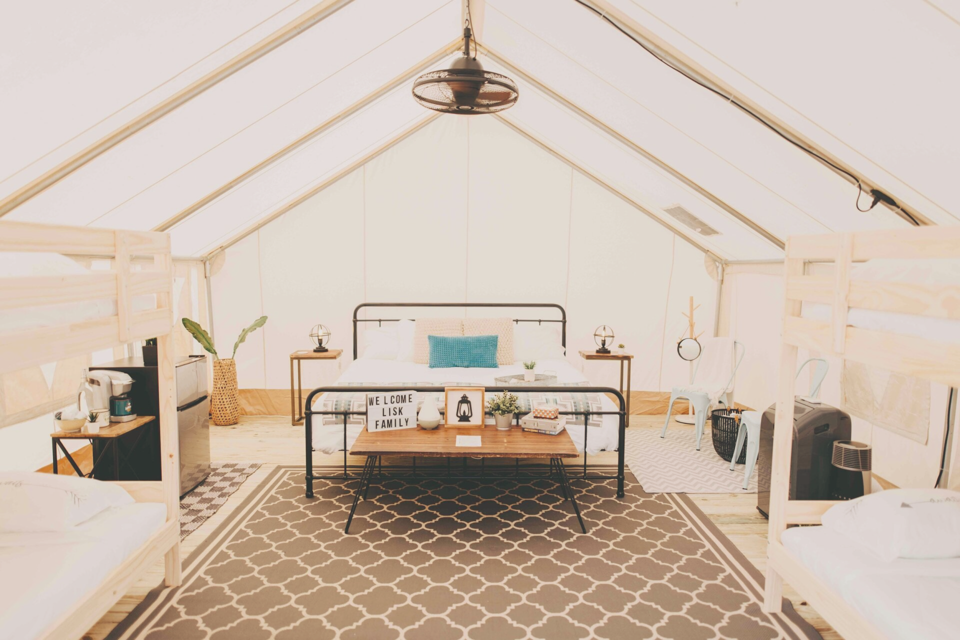 Spacious glamping tent interior with bed, bunk beds, rugs, coffee station, and a fan.