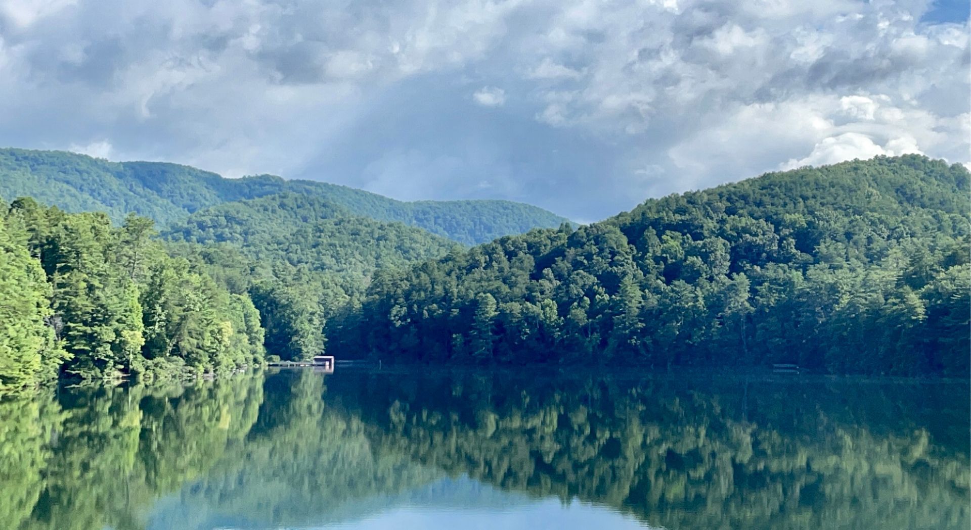 Lake reflecting green mountains and a cloudy sky.