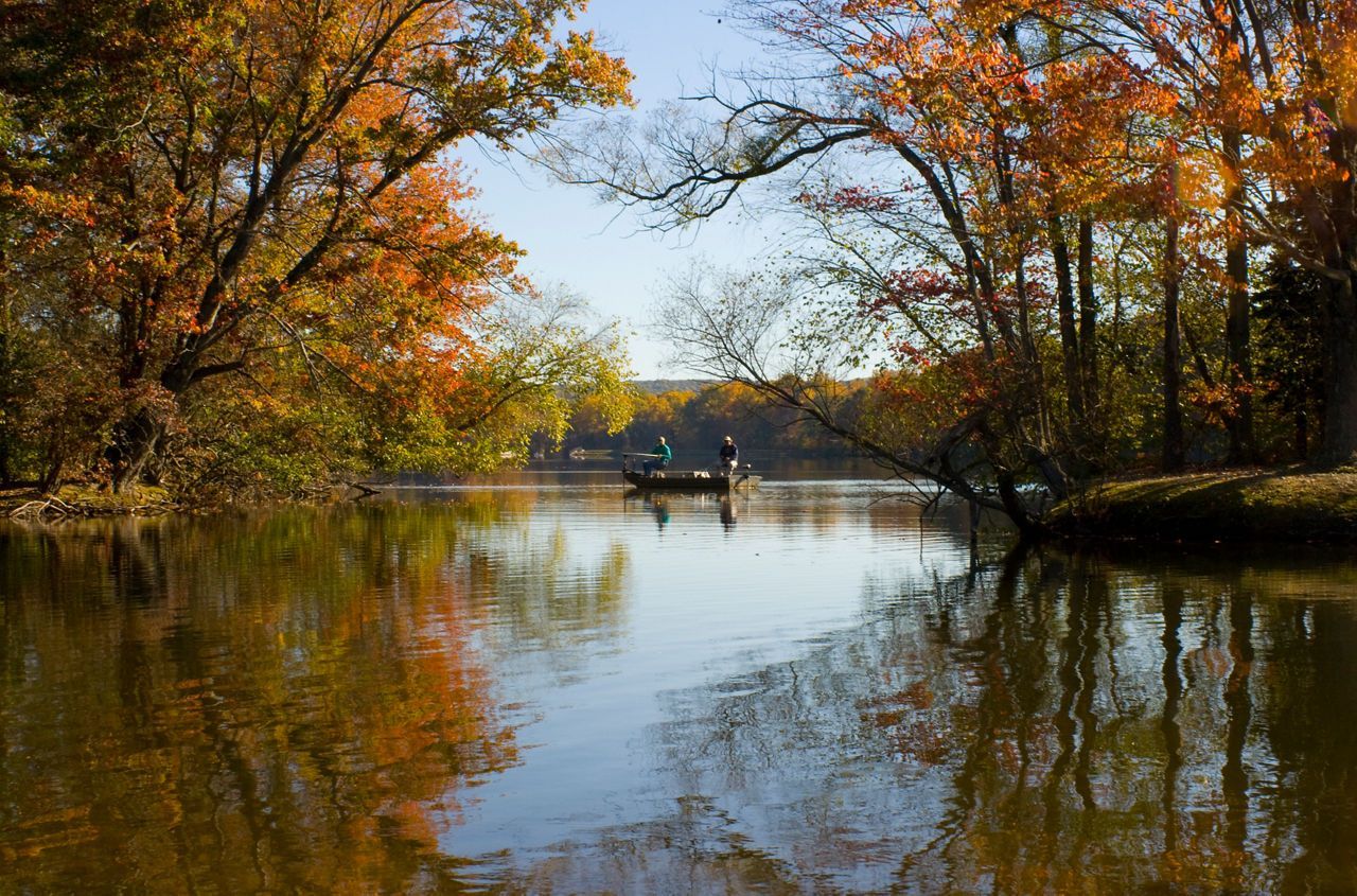 Calm river scene with fall foliage framing a small boat, reflecting in the water.