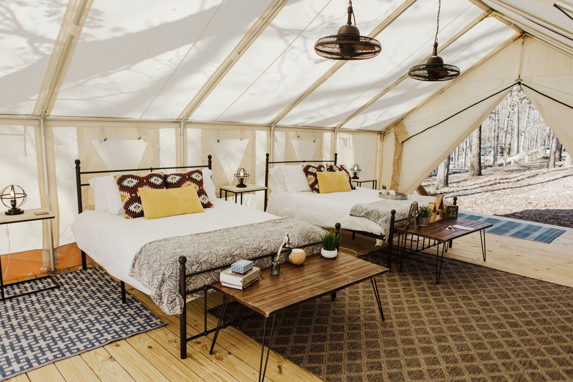 Large canvas tent interior with two beds, small tables, rugs, and overhead fans.