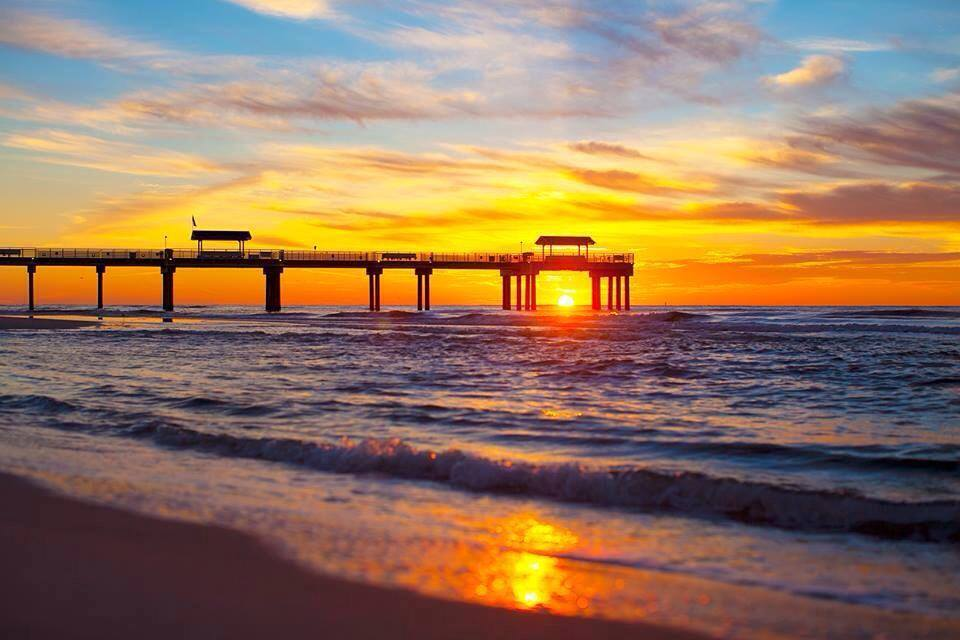 Pier silhouetted against a vibrant sunset over the ocean, reflecting golden light on the water.