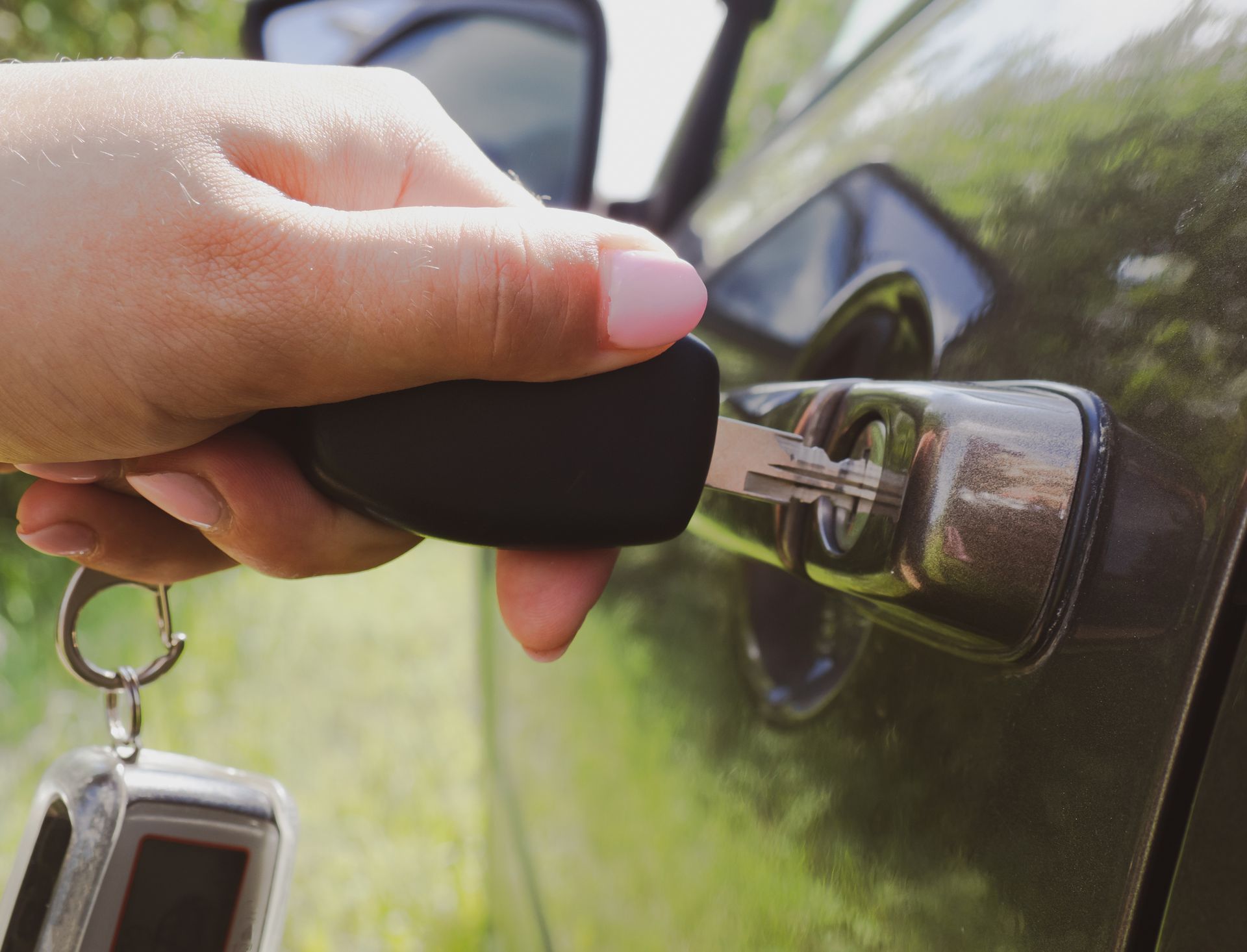 A woman is holding a car key in her hand and opening the door of a car.