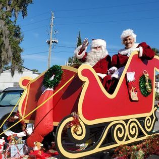 Two santa clauses are riding in a sleigh in a parade.