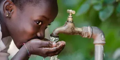 A young girl is drinking water from a faucet.