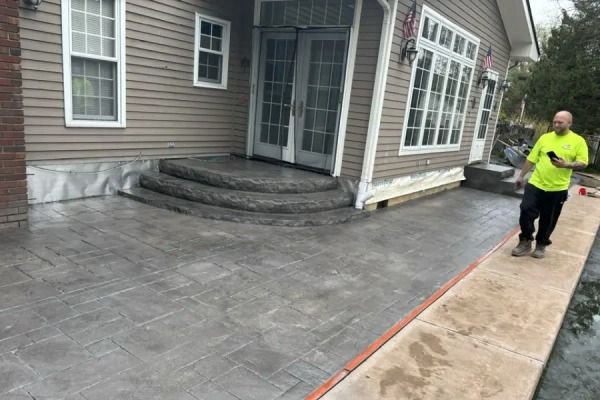 Patio pavers being installed beside a house, with a worker in a neon shirt on the sidewalk