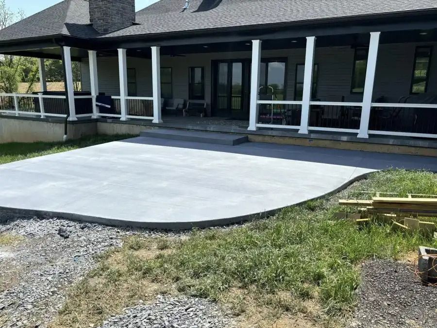 Covered patio with white concrete slab in front of a dark house with white columns
