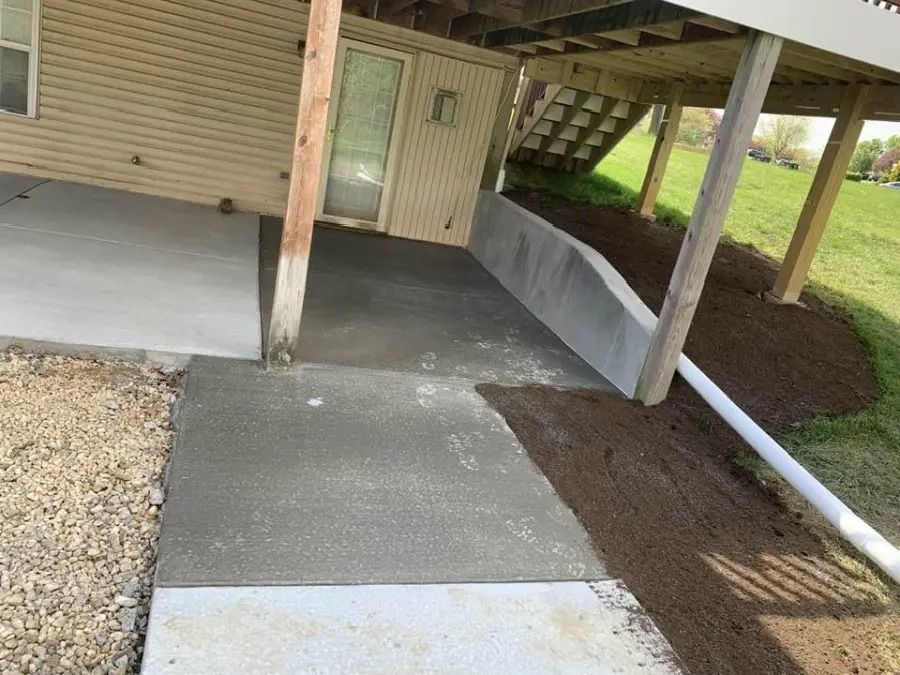 Covered concrete walkway and ramp leading to a house entrance with handrails and gravel beside it.