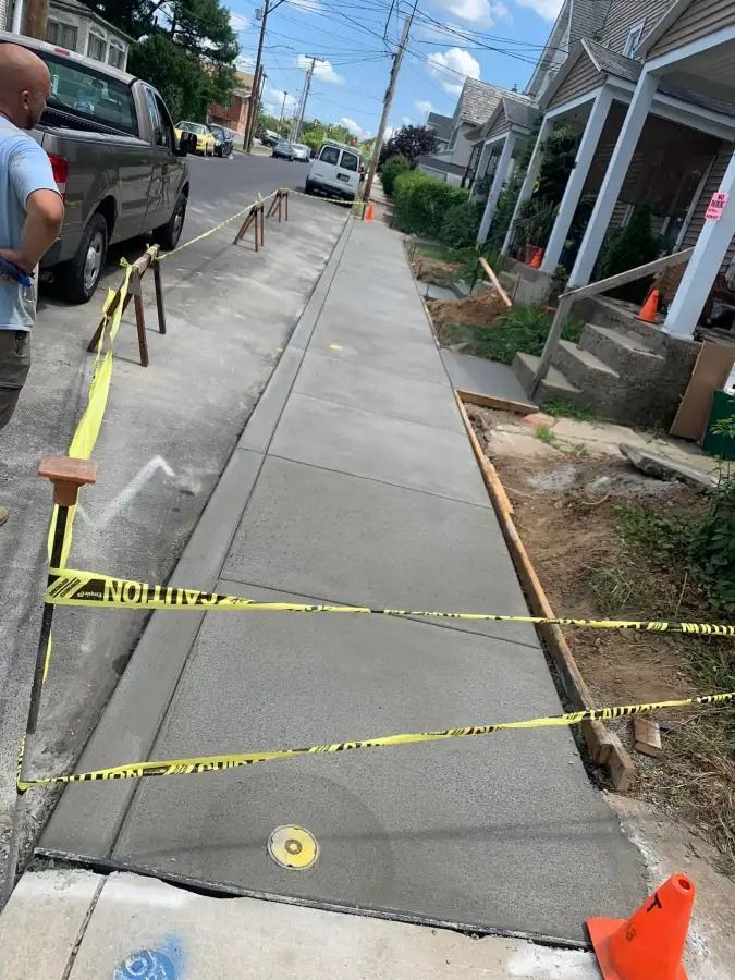 Sidewalk under repair with caution tape, cones, and fresh concrete along a residential street