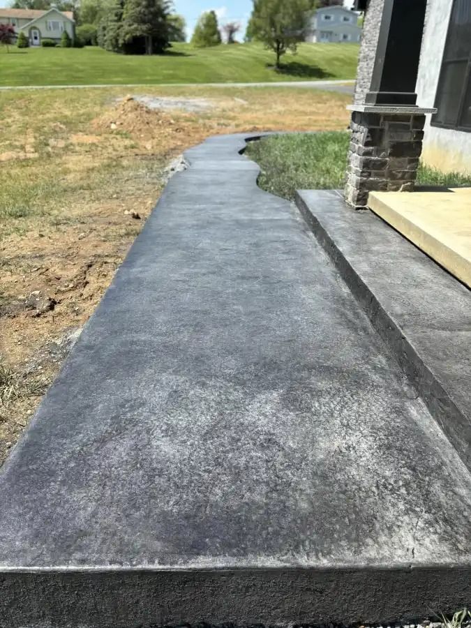 Freshly paved black concrete walkway beside a house leading to a grassy yard