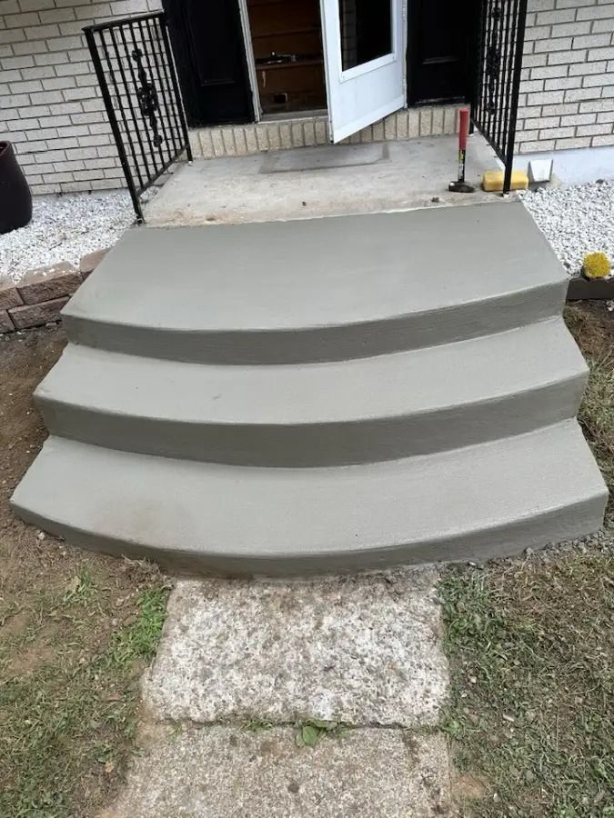 Three gray concrete front steps leading to a porch with an open door and black railings.