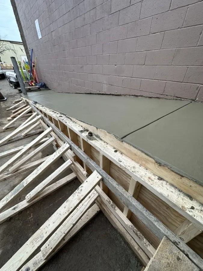 Construction site with a concrete slab poured along a pink cinderblock wall and wooden formwork below