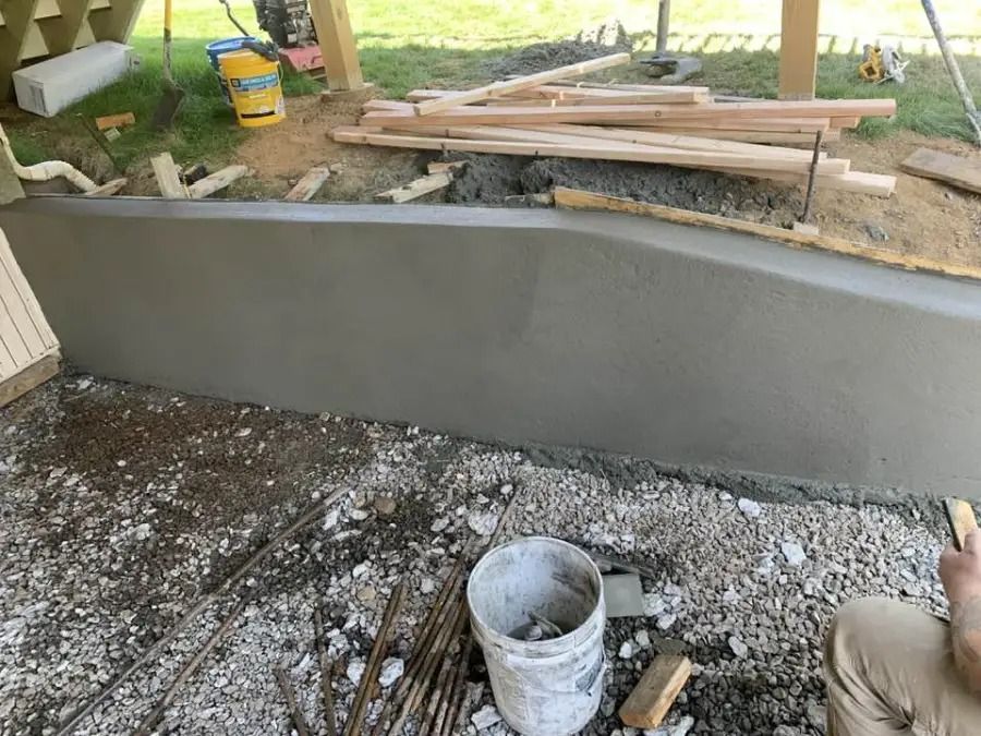 Curved gray concrete retaining wall under construction beside a yard, with tools and lumber nearby