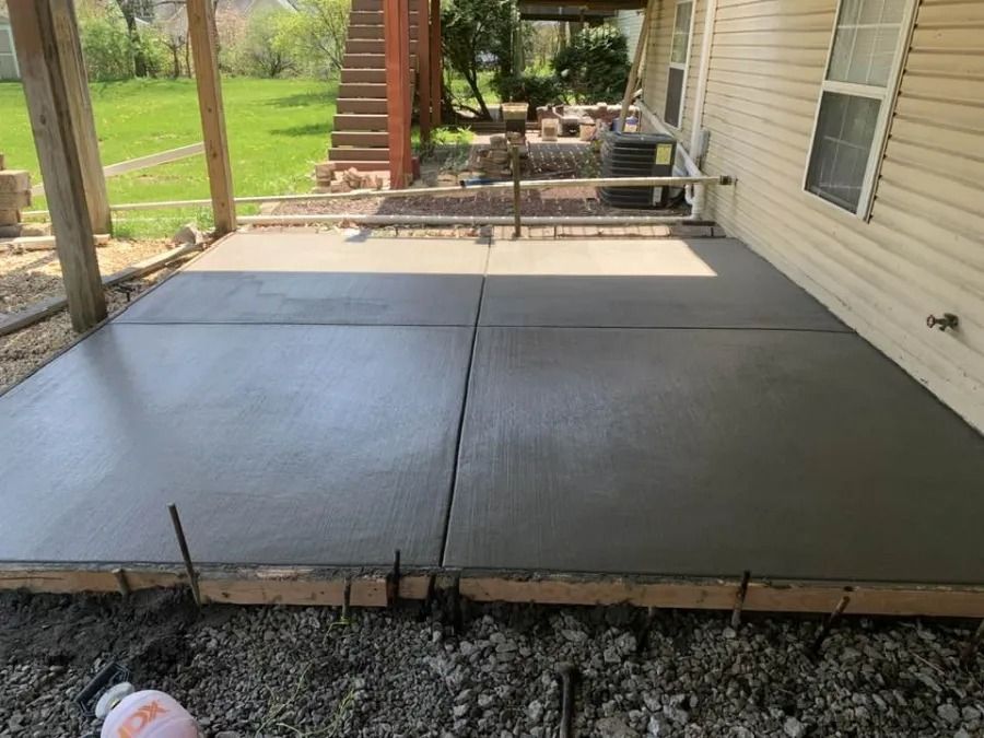Freshly poured concrete patio beside a house, with wooden forms and a covered porch in the background