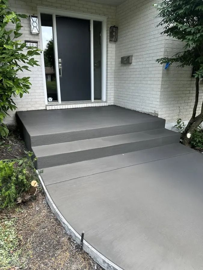 Concrete ramp and steps leading to a front door of a white brick house.