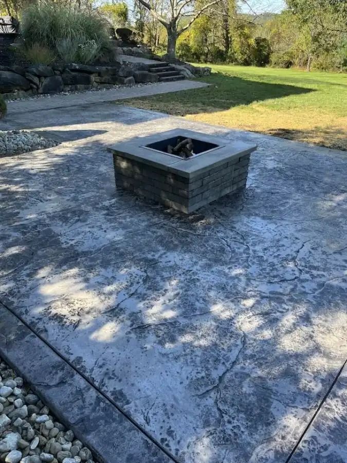 Stone fire pit centered on a sunlit patio with lawn and steps in the background