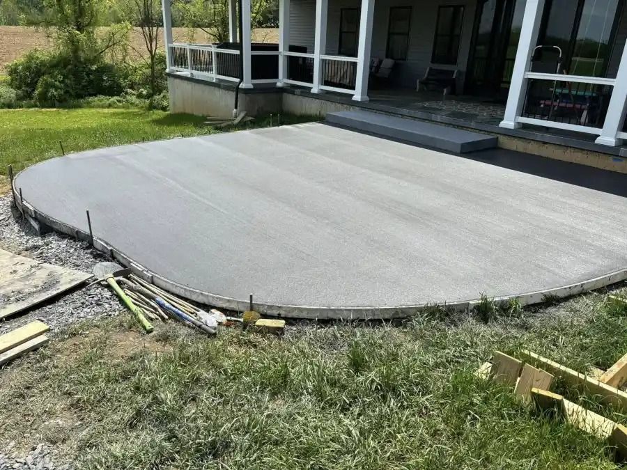 New concrete patio slab beside a house, with construction materials around the edge