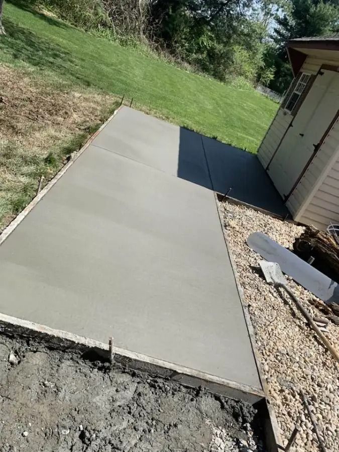 Concrete walkway beside a house, bordered by grass and gravel, under bright sunlight.
