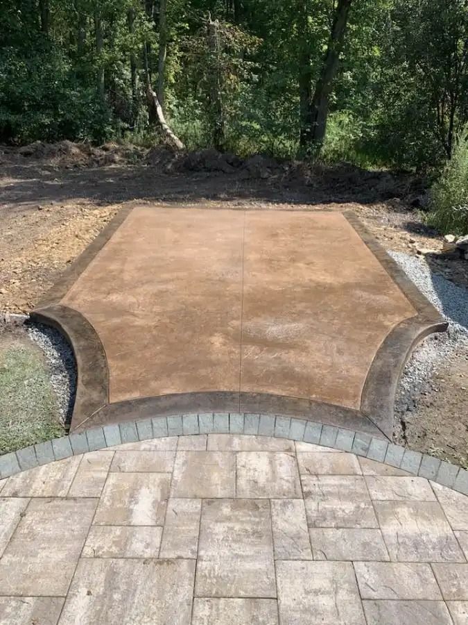 Empty concrete patio with brick border and wooded garden behind it