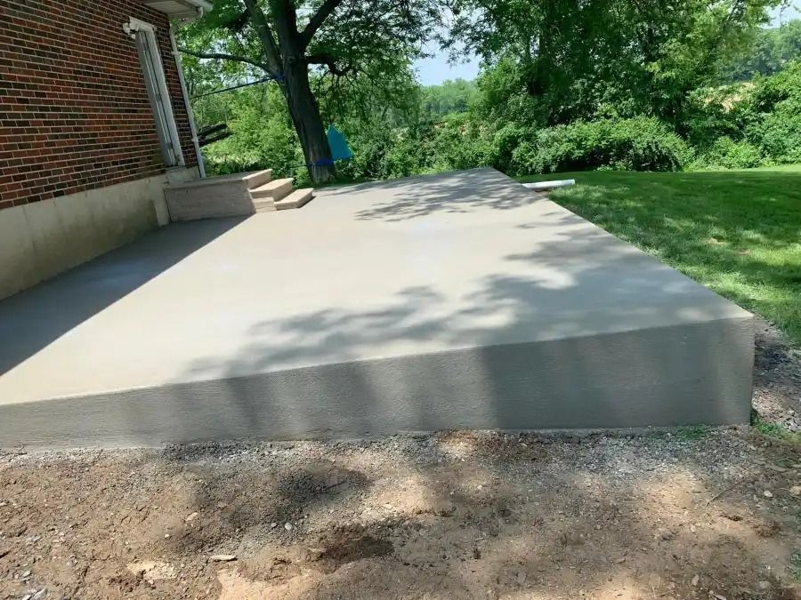 Concrete patio beside a brick building, with trees and grass in the background.