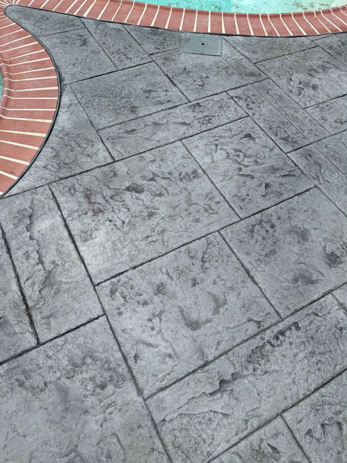 Gray stone patio with brick border and a curved strip of green and white tiles
